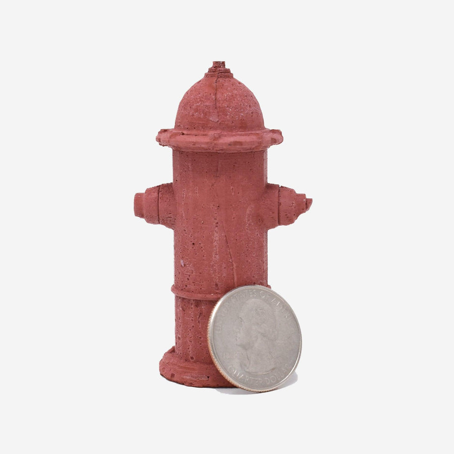 The back of a 1:12 scale miniature red-dyed concrete fire hydrant with a quarter sitting on the side showing the scale